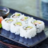 California roll on blue rectangular plate with wasabi, ginger and soy sauce.  Shot with shallow focus on front sushi.
